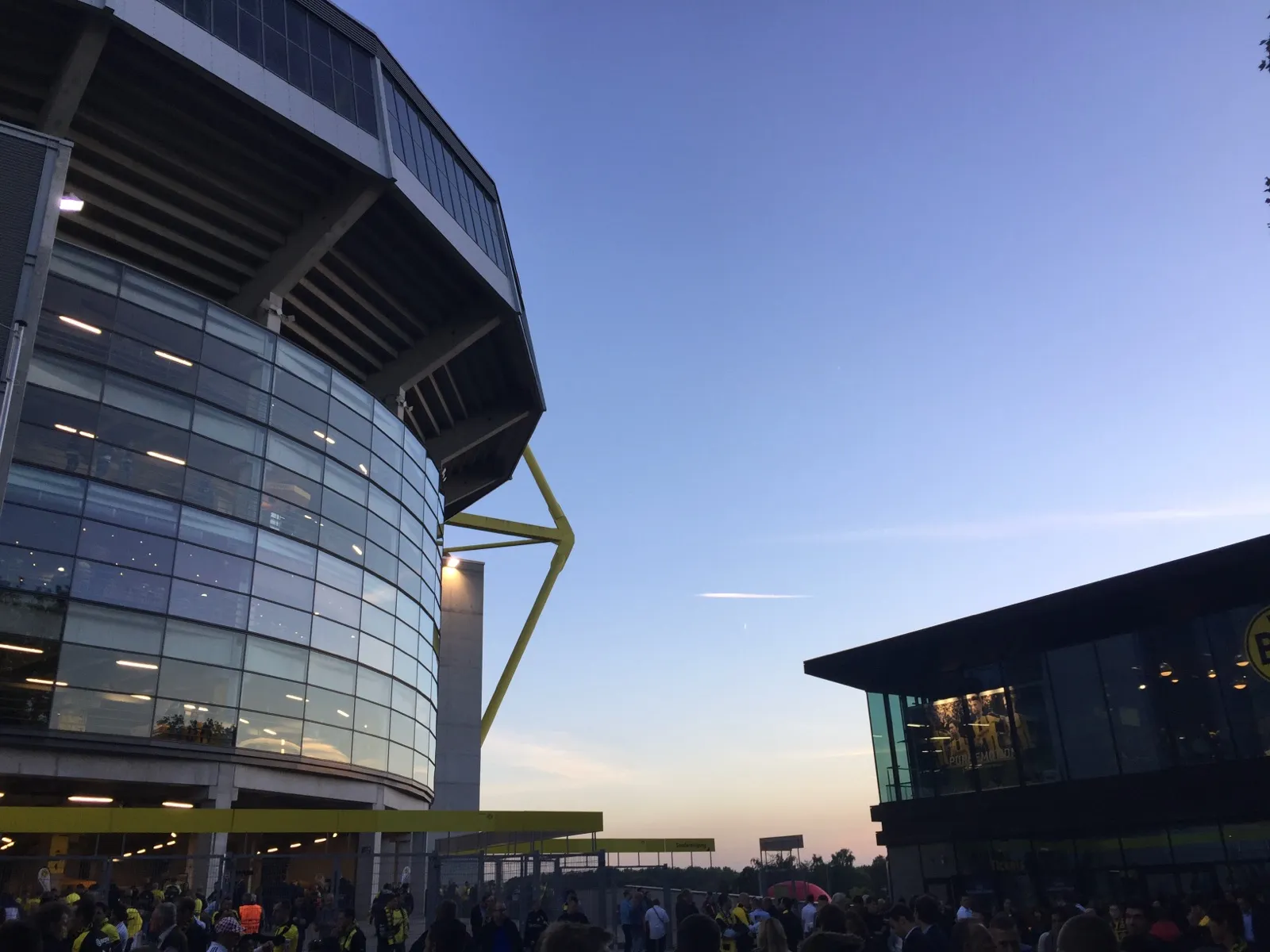 Glasfassade und gelber Pylon des Signal Iduna Park in der Abenddämmerung, rechts die BVB-FanWelt